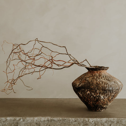 The Oran artisan pottery vase, with its rustic texture, displays dry, twisted branches on a stone surface against a neutral beige background—an understated accent for home decor.
