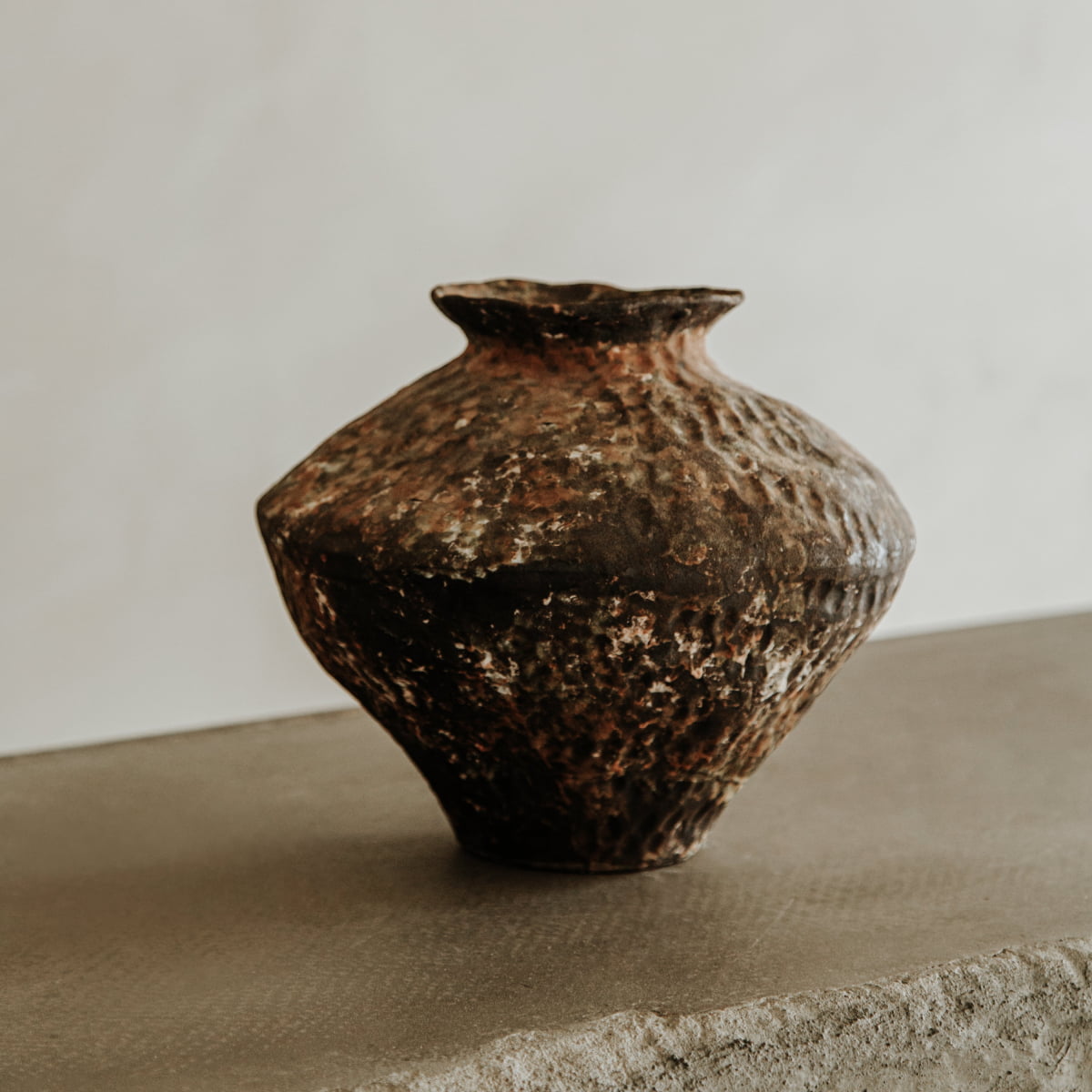 The Oran ceramic vase features a rustic, textured finish with an organic, uneven shape and earthy brown tones. Ideal for home decor, it stands out on any surface against a neutral background.