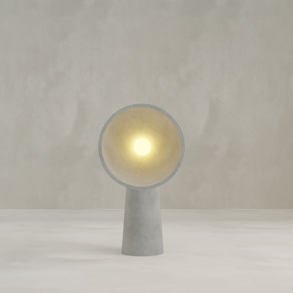 The Orbis Medium Floor Lamp features a minimalist concrete design with a cone-shaped base and circular shade, casting a soft glow against a light background—a sophisticated tribute to sculptural artistry.