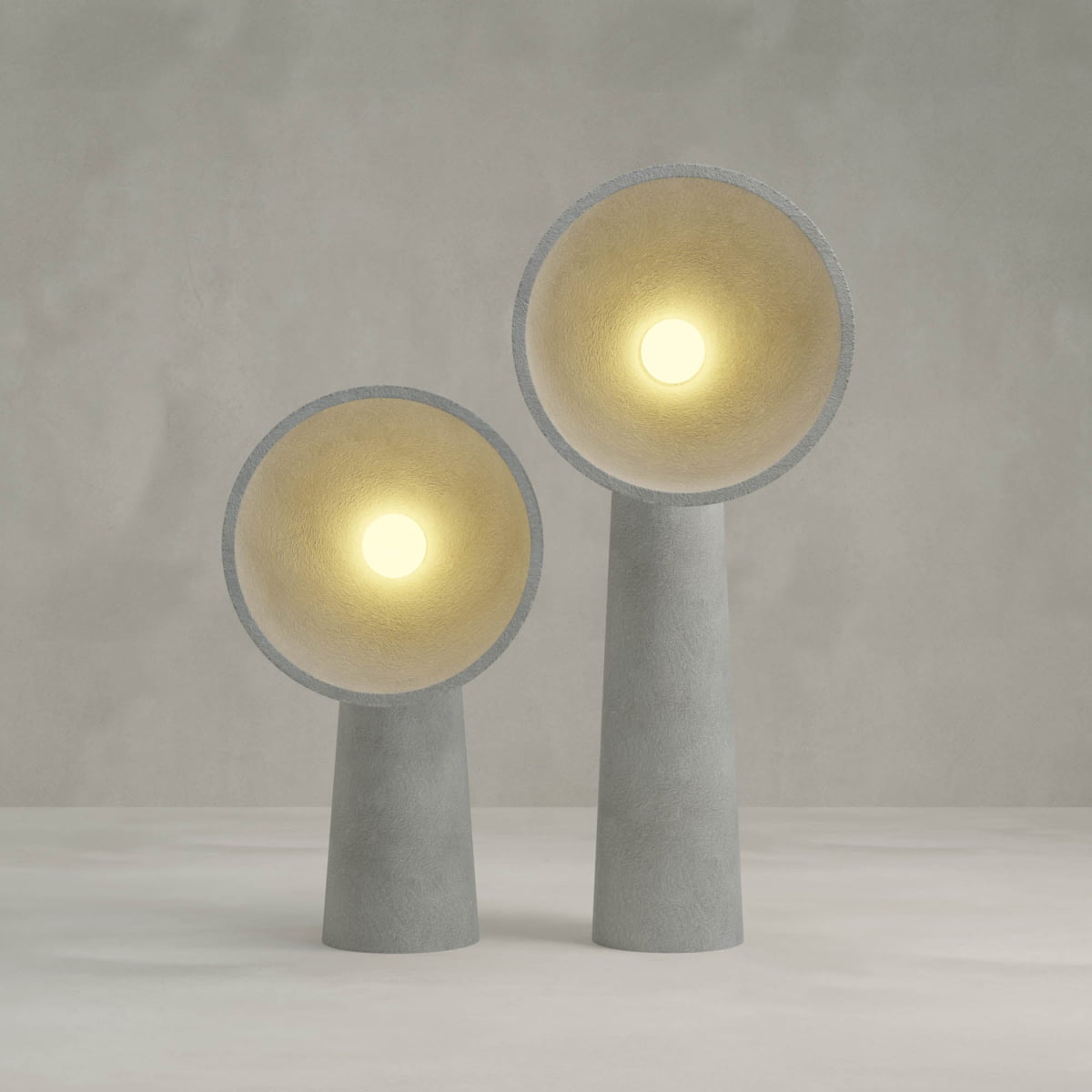 The Orbis Medium Floor Lamp features a modern cone silhouette with a gray cylindrical natural stone base and a wide circular shade, casting soft yellow light that blends sculptural artistry with refined organic style.