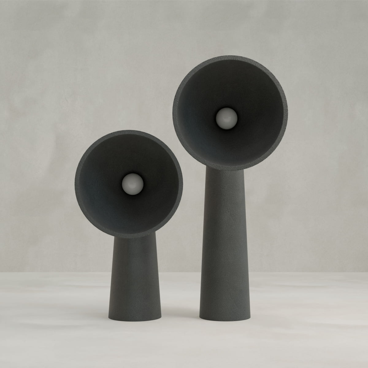 Two Orbis Medium Floor Lamps, featuring modern black designs with conical bases, wide flared tops, and a central sphere in each opening, stand side by side against a plain light gray background.