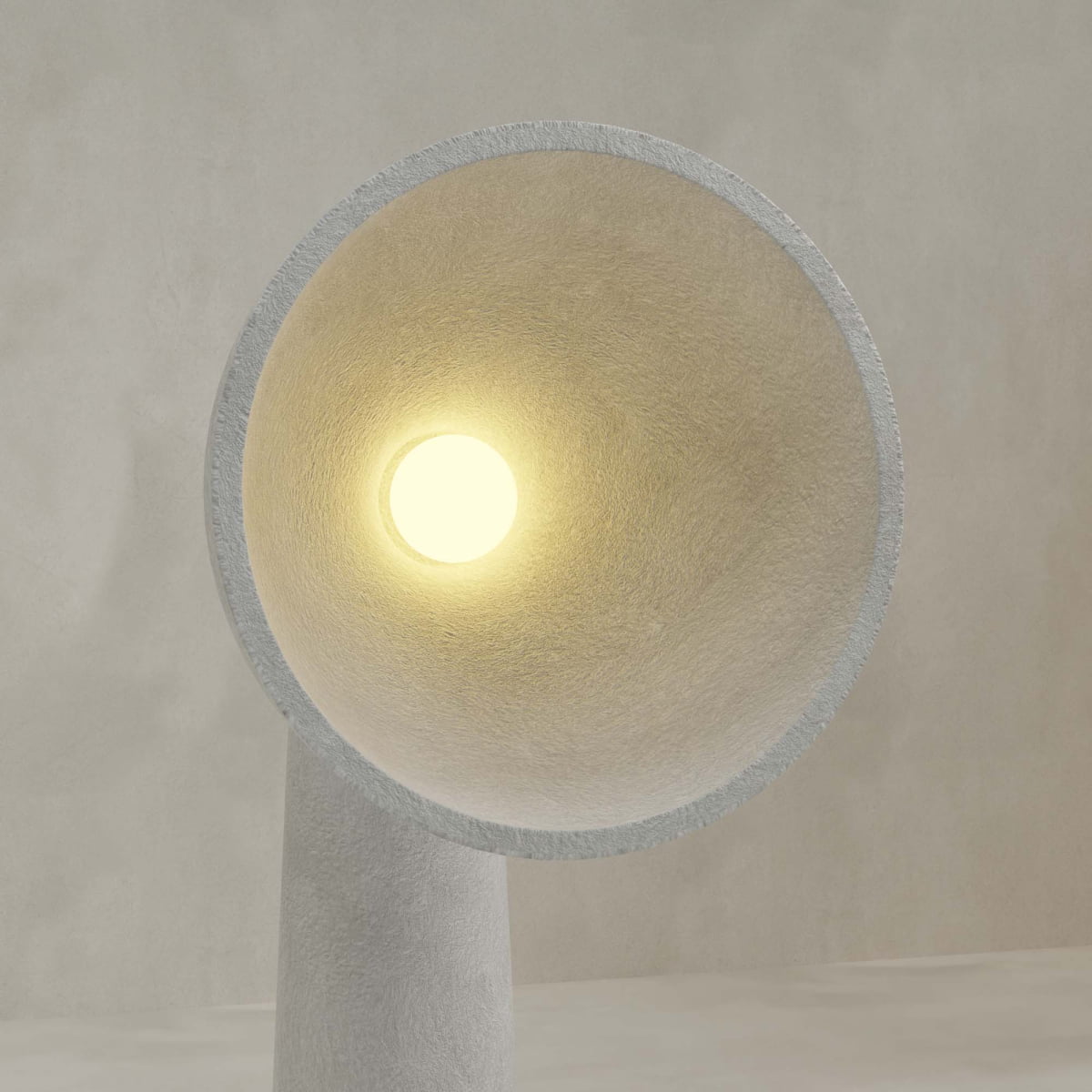 A close-up of the Orbis Tall Floor Lamp reveals its modern, textured design with a wide conical shade and glowing bulb, highlighting sculptural artistry against a plain, light background.