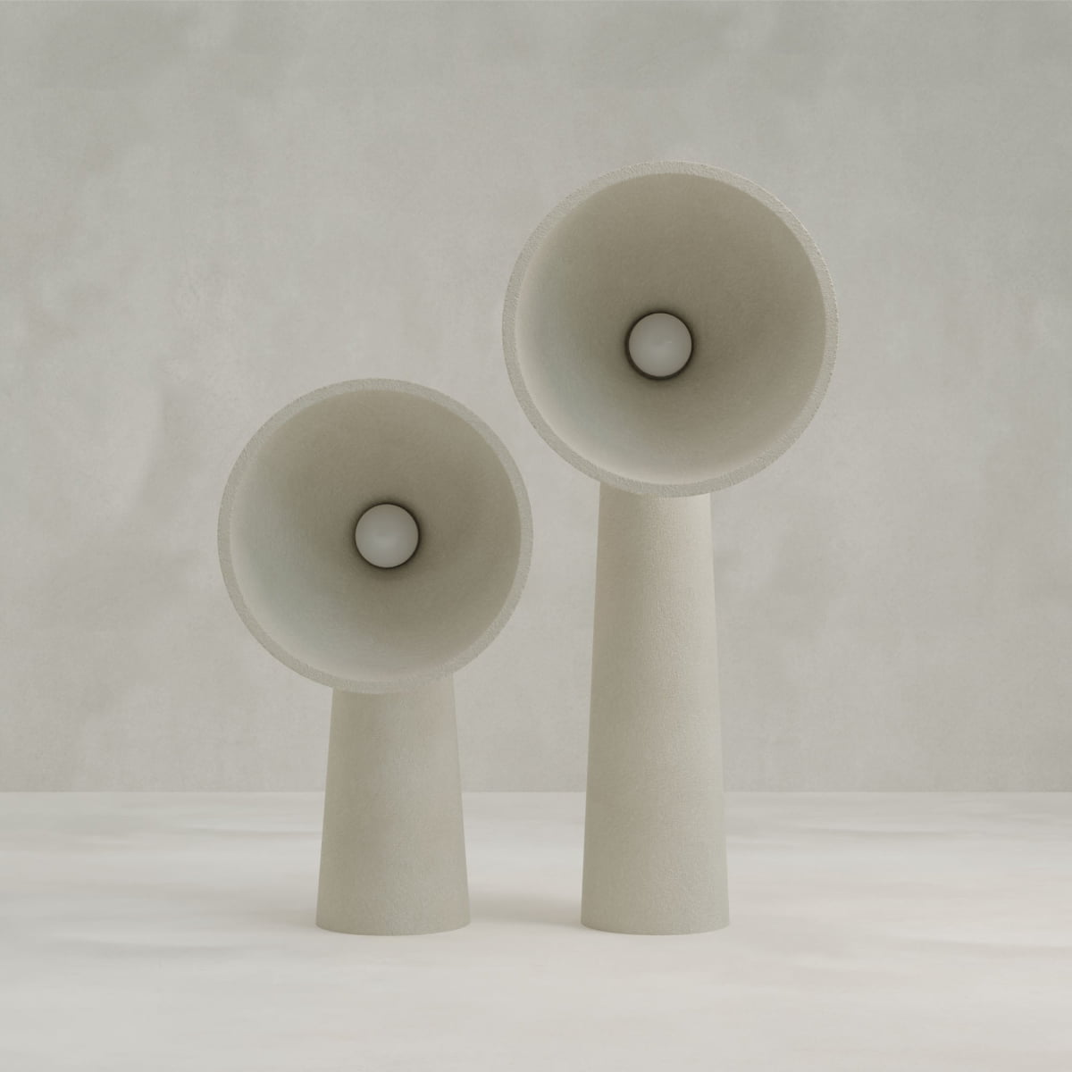 Two Orbis Tall Floor Lamps in modern beige, featuring cone-shaped shades with circular bulbs and round bases, stand on a light surface against a neutral backdrop, highlighting their sculptural design.