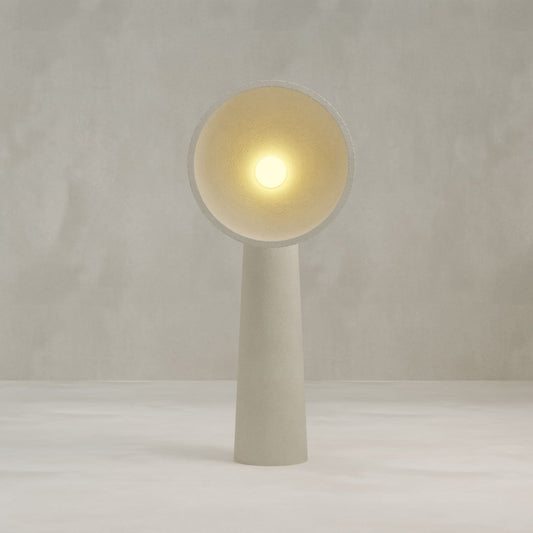 The Orbis Tall Floor Lamp is a minimalist, modern piece with sculptural artistry, a cylindrical base, and a wide circular shade that emits soft yellow light, set against a plain, light-colored background.