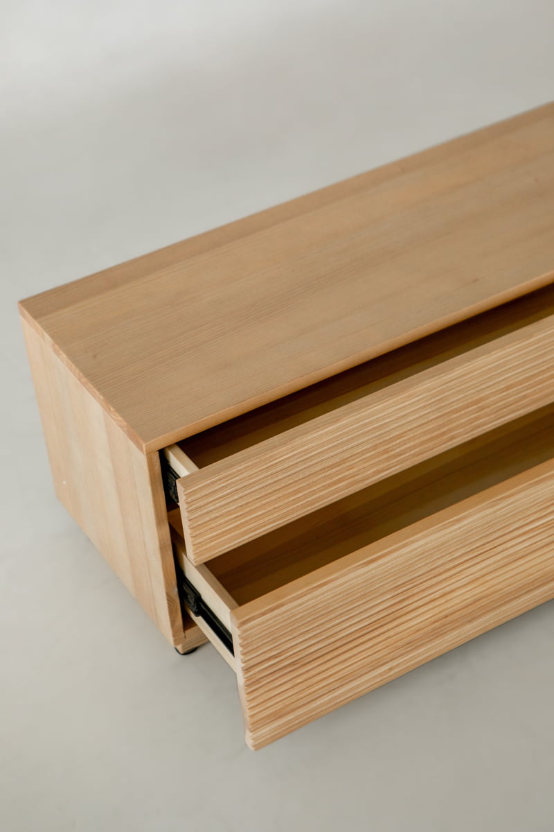 A close-up of the Oster Media Console reveals discreet drawers partially open, highlighting its simple, clean lines and minimalist design against a plain background.