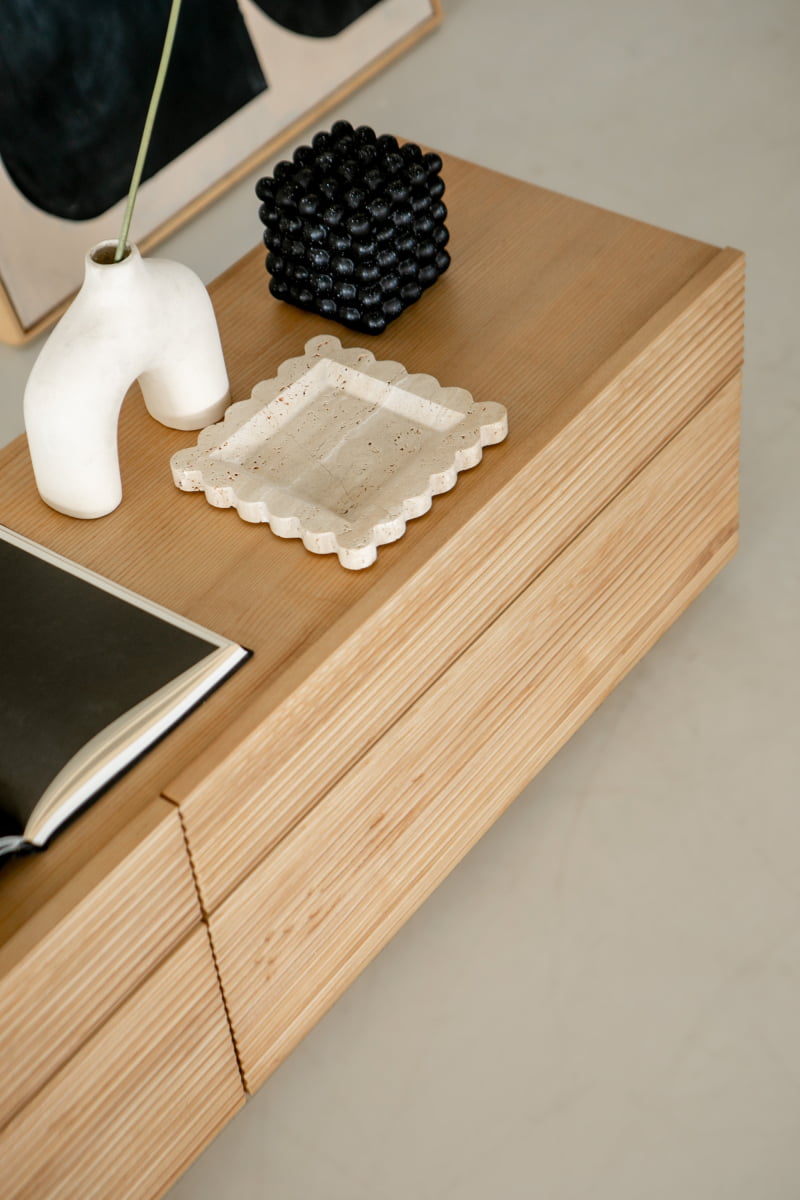 The Oster Media Console showcases minimalist style, topped with a white abstract vase holding a stem, a black textured sculpture, a scalloped stone tray, and an open book arranged neatly.