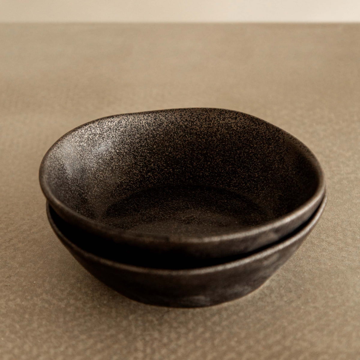 Two Pebble Speckled Bowl Large ceramics are stacked on a neutral, subtly textured surface with a plain background.