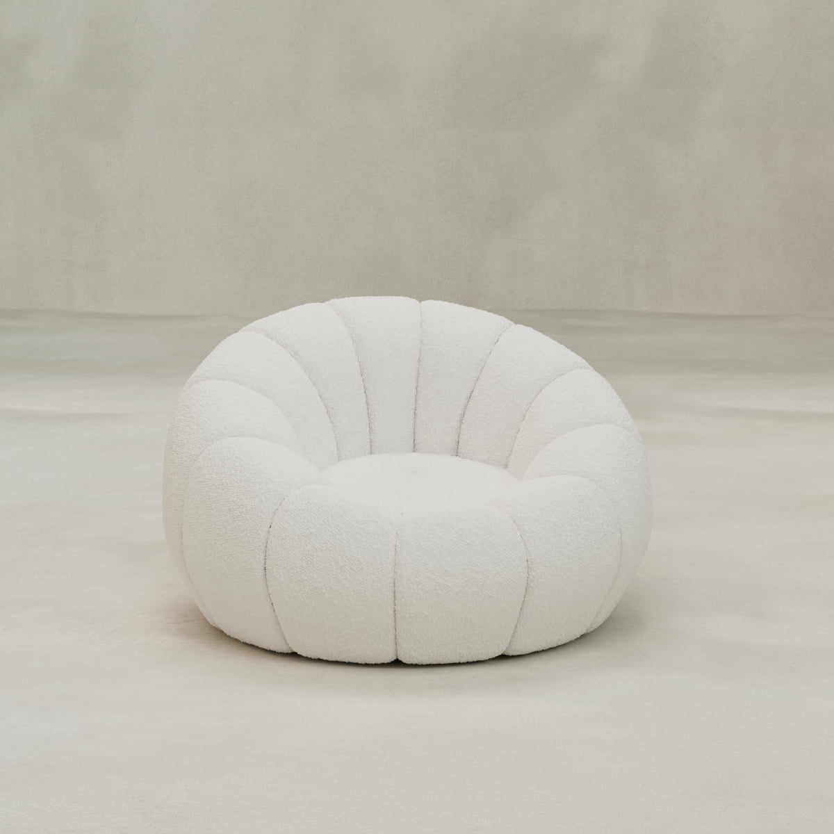 A modern, round Penelope Chair with Ottoman in white bouclé features a scalloped, segmented design for cozy comfort, displayed on a smooth, light floor against a neutral backdrop.