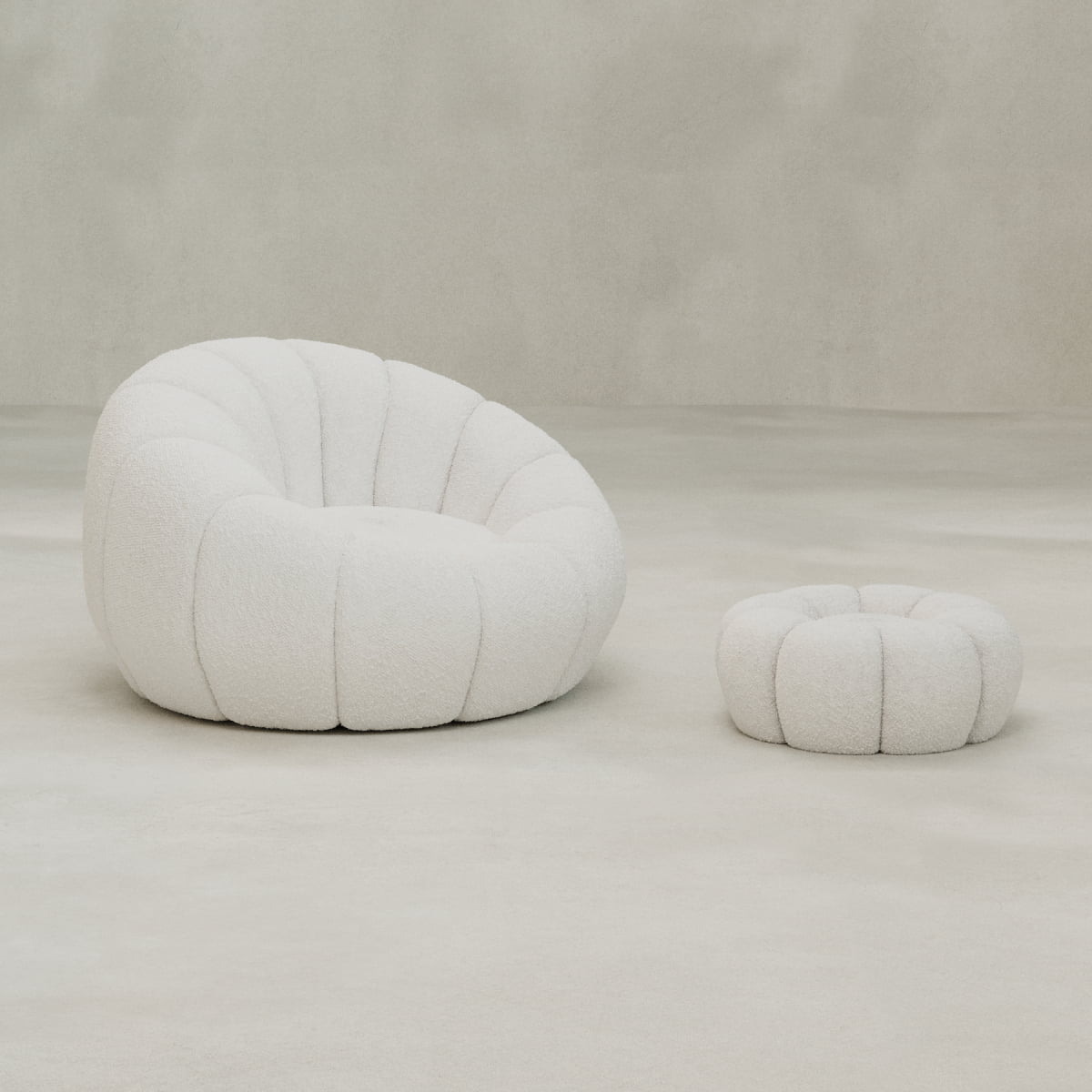 The Penelope Chair with Ottoman, in plush white bouclé fabric and soft tufting, offers inviting comfort. Both pieces rest on a light grey floor against a neutral backdrop, creating a cozy and stylish look.