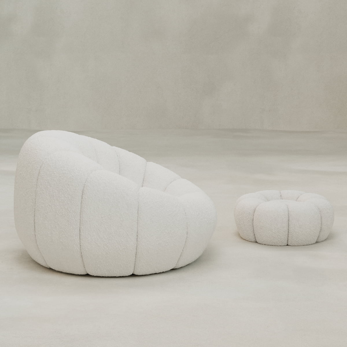 The Penelope Chair with Ottoman, featuring plush white bouclé fabric, sits on a light floor against a neutral backdrop, creating an inviting sense of cozy comfort.