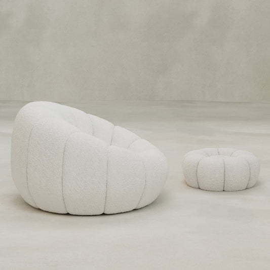 The Penelope Chair with Ottoman, featuring plush white bouclé fabric, sits on a light floor against a neutral backdrop, creating an inviting sense of cozy comfort.