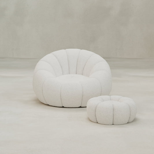 The Penelope Chair with Ottoman features plush, tufted bouclé upholstery in white. Set on a minimalist background, this cozy duo offers inviting comfort perfect for relaxation.