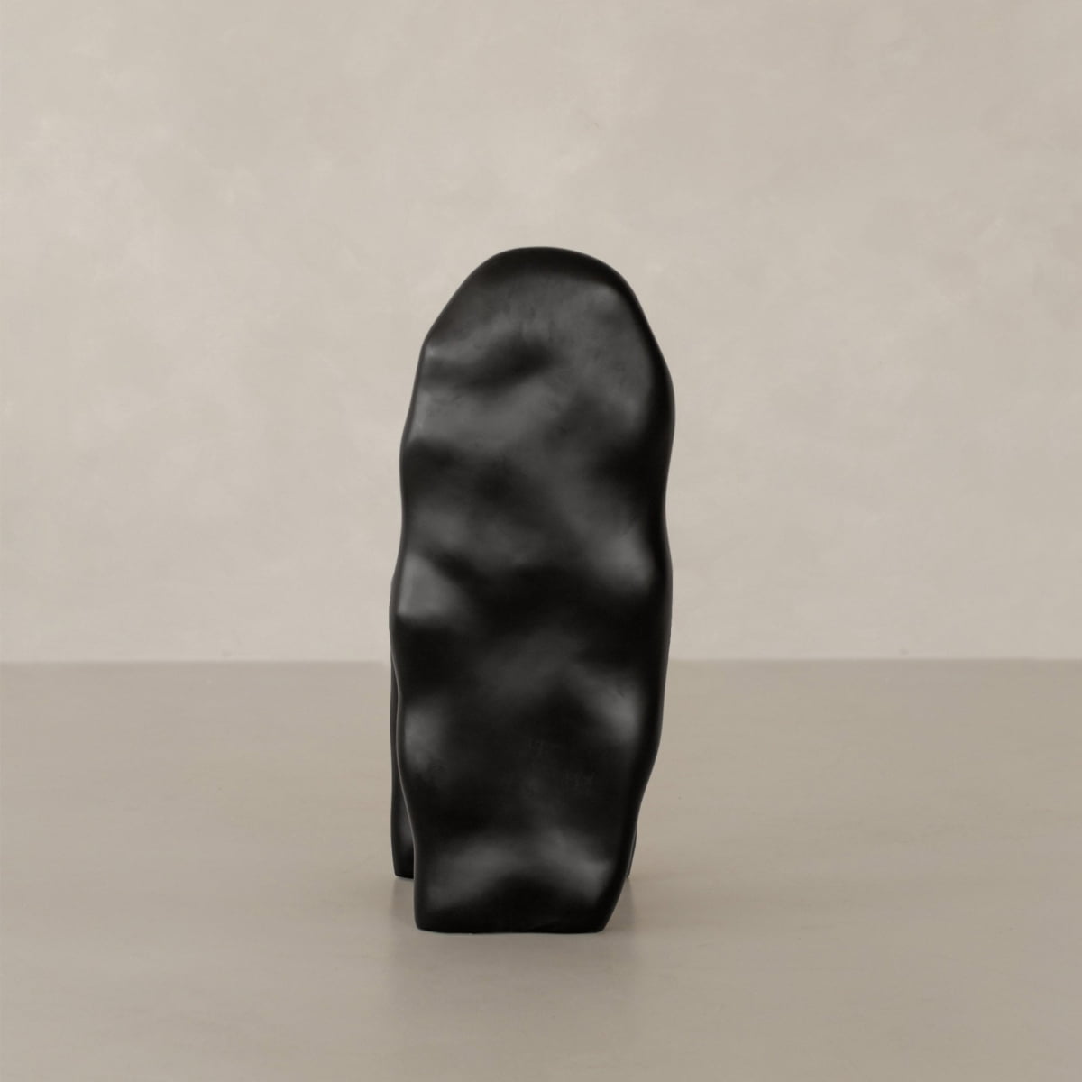 The Phantom Chair Rental features a smooth, abstract black form with gentle curves and irregular surfaces, standing upright on a light gray surface—a showcase of modern design against a pale, textured backdrop.