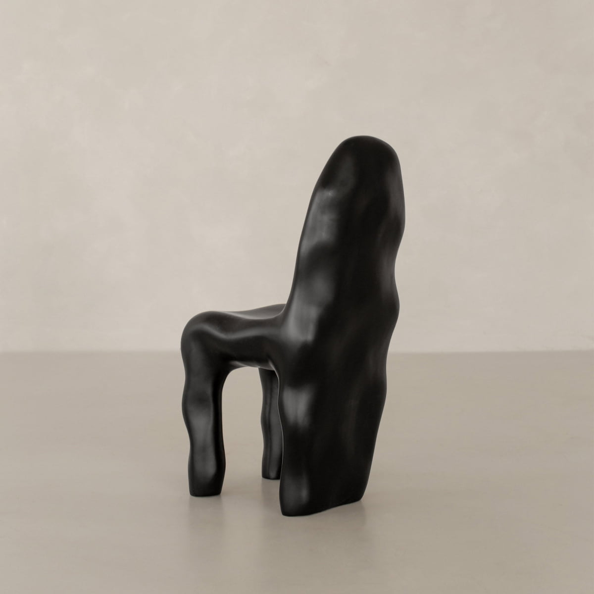 The Phantom Chair Rental features sculptural, organic wavy curves and an uneven black surface. It stands on a smooth, light floor with a plain, neutral backdrop, showcasing modern craftsmanship.