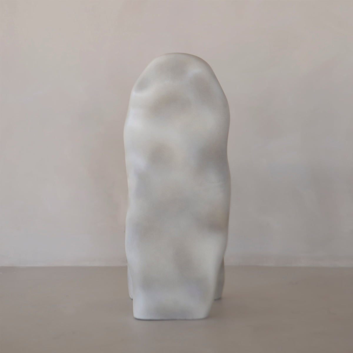 The Phantom Chair Rental features a smooth, abstract upright form with a rounded top and subtle grayish tones, echoing brutalist design and refined modern craftsmanship against a plain, light-colored background.