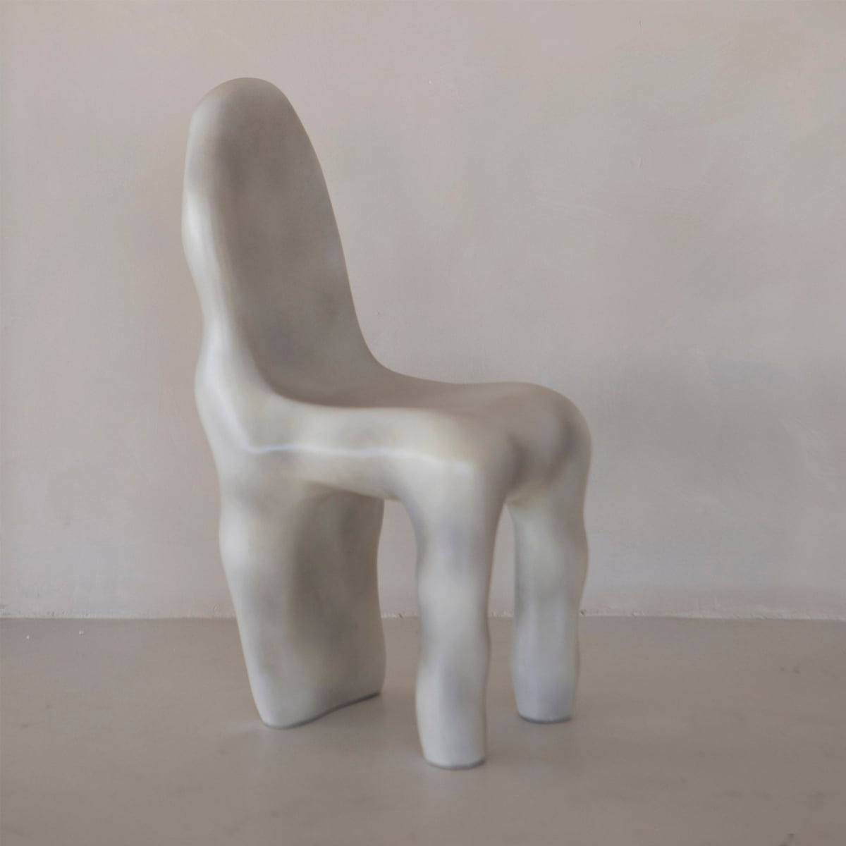 The Phantom Chair Rental is a sculptural, brutalist-inspired chair with an abstract organic form, smooth pale gray surface, rounded edges, and uneven leg-like supports—perfect for making a statement against a plain light background.