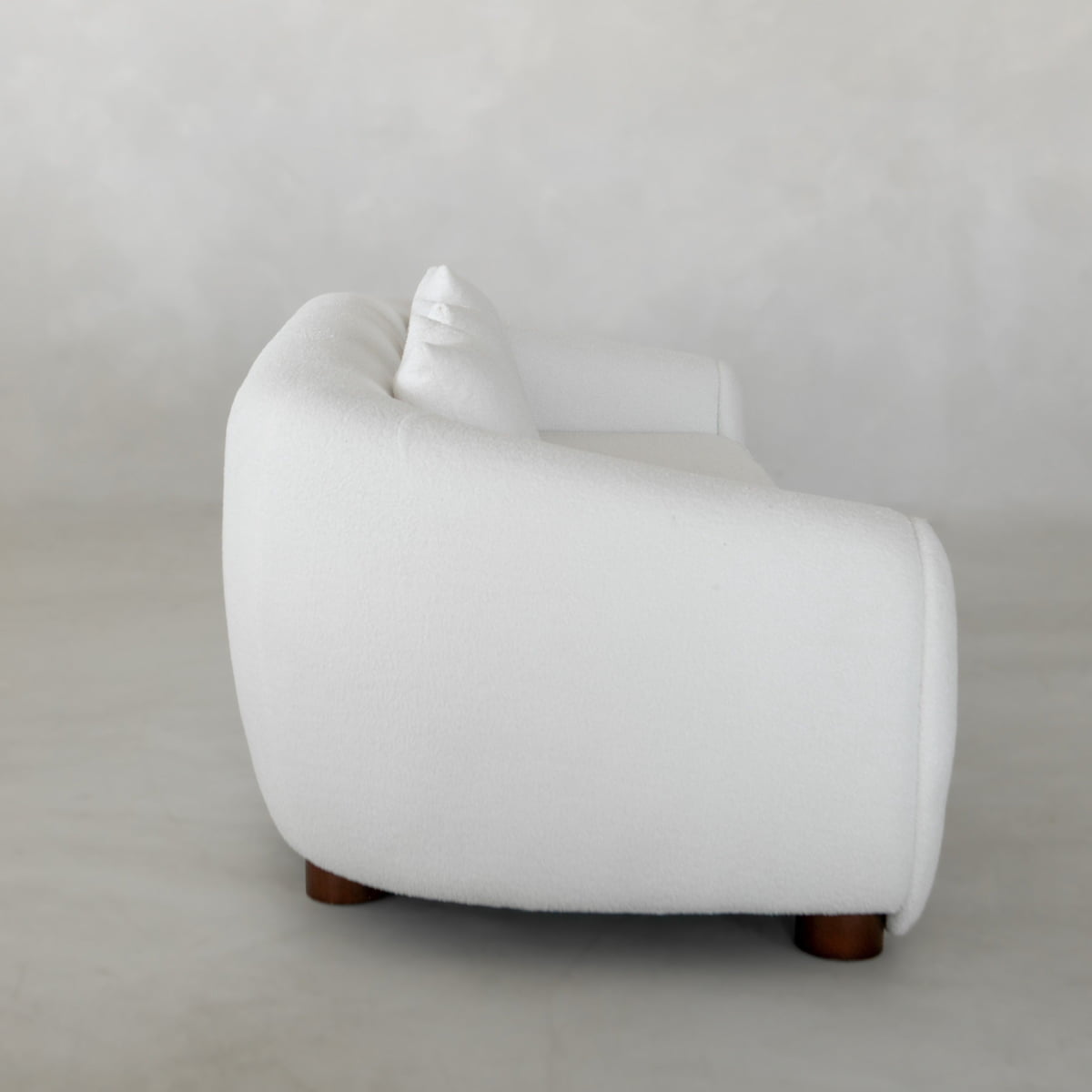 The Polar Bear Armchair is a modern white upholstered chair with rounded edges and wooden legs, showcasing contemporary design, shown in a side view against a light textured background.