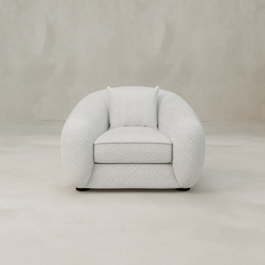 The Polar Bear Armchair features modern, rounded design with plush cushioning and light grey fabric, evoking cozy style against a plain, light-colored background.