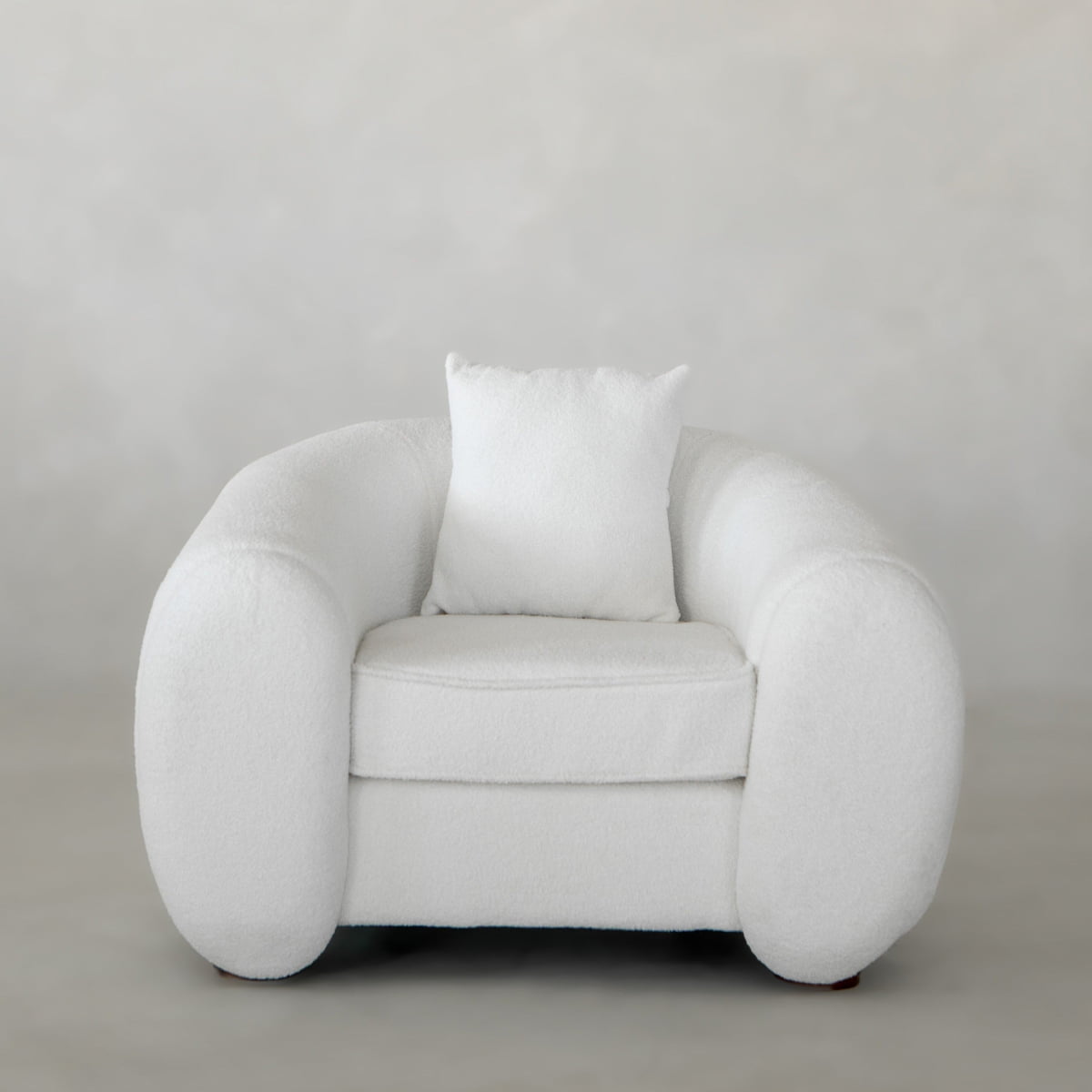 The Polar Bear Armchair, plush and white with a matching square pillow, sits on a neutral floor against a soft light gray background, showcasing contemporary design and modern aesthetics.