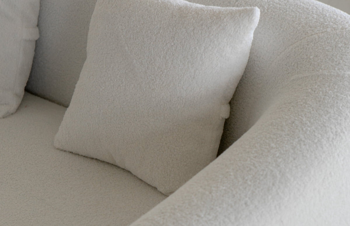 A close-up of the Polar Bear Sofa shows its soft, textured cream upholstery and a matching square cushion against the curved armrest—a refined blend of contemporary design and luxury.