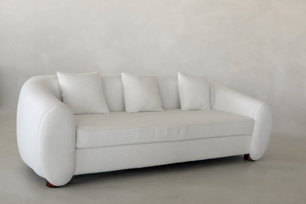 The Polar Bear Sofa, featuring rounded arms and four matching square pillows, adds a touch of luxury and contemporary style to your living space with its modern design.