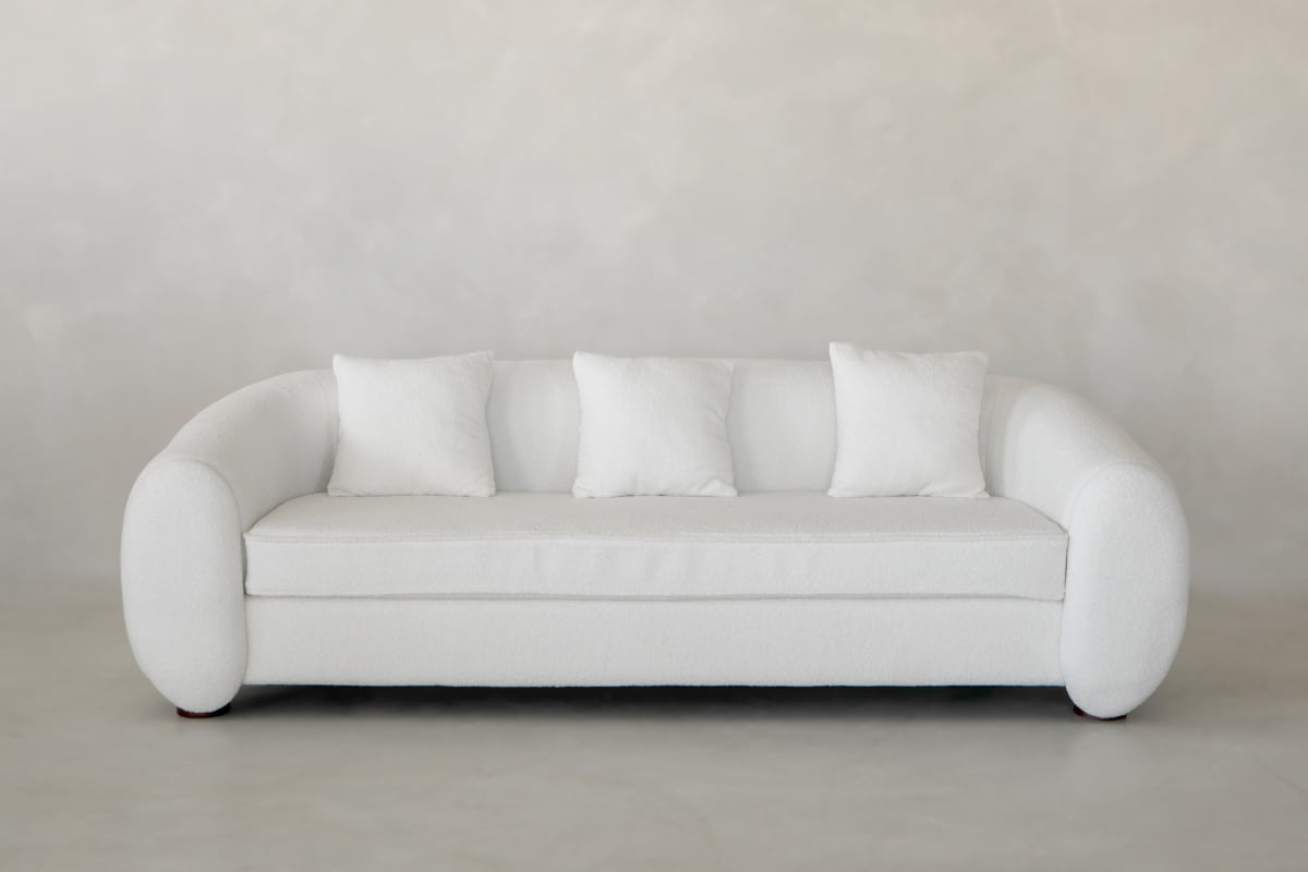 The Polar Bear Sofa is a modern white set with rounded arms and four matching cushions, adding contemporary luxury to any space with a light gray textured wall and floor.