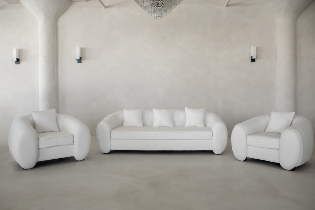 A minimalistic living room showcases a Polar Bear Sofa and two matching armchairs with rounded arms, set against a light textured wall with sconces and columns for a modern, luxurious, and clean look.