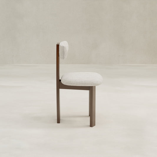 The Radley Dining Chair features a soft, rounded white bouclé seat and backrest with a minimalist wooden frame, shown in profile against a neutral light background.