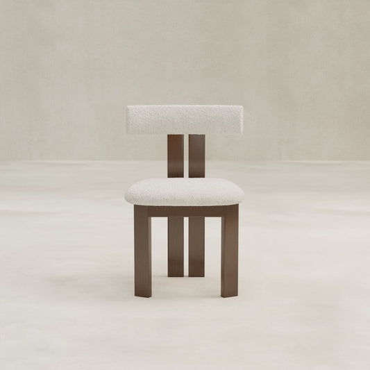 The Radley Dining Chair features a brown wooden frame with square legs, a minimalist design, and padded white bouclé fabric on the seat and rectangular backrest—perfect for adding comfort to any neutral, light-toned room.