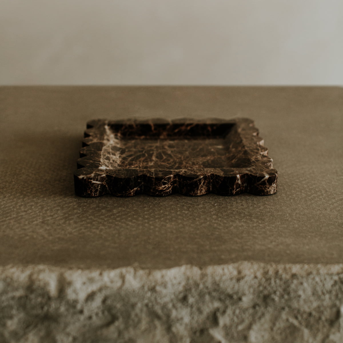 The Remy Tray In Marble features scalloped edges and a textured stone surface, adding modern elegance to any space with its sophisticated design and neutral tones.
