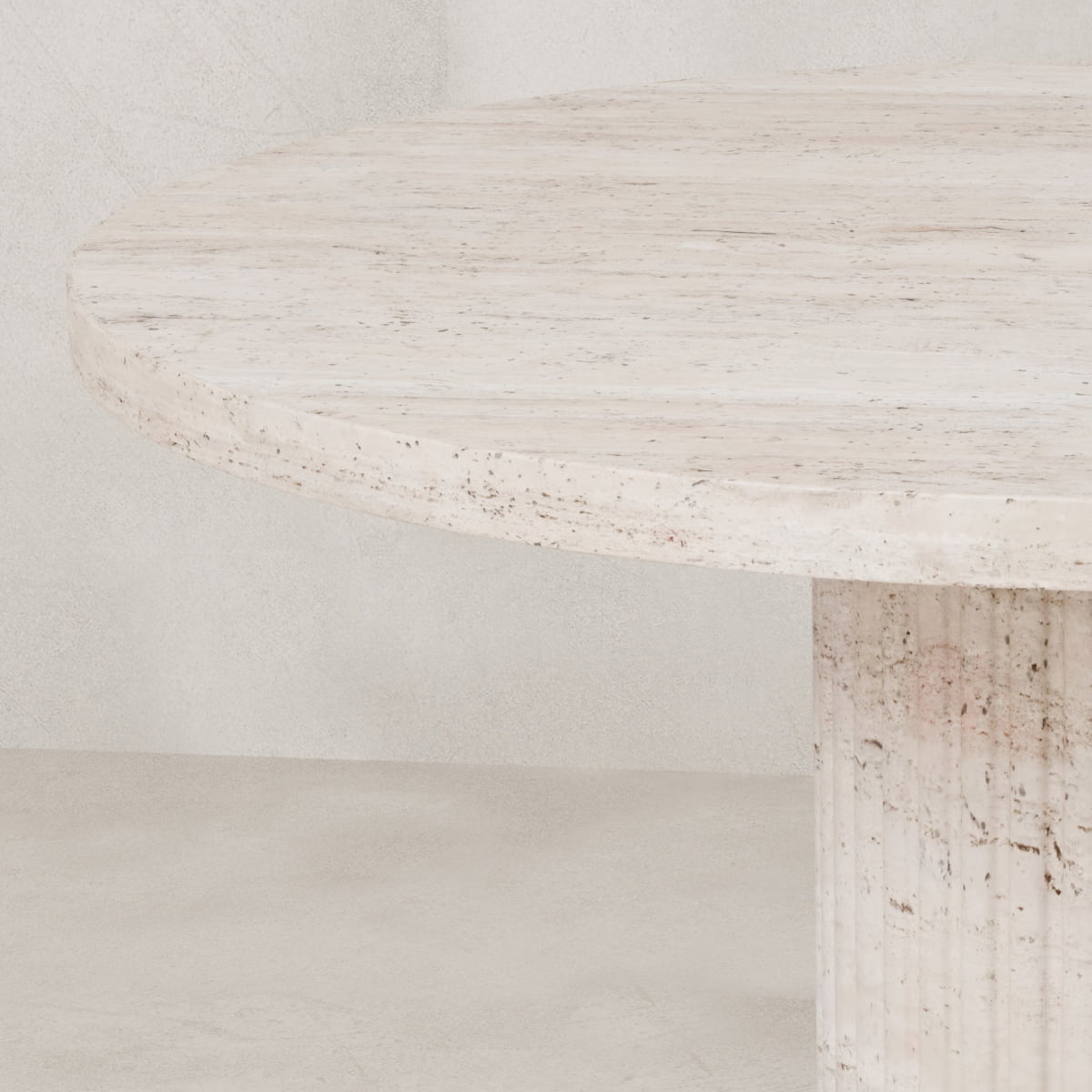 A close-up of the Richmond Table: a round, light beige travertine dining table with a textured surface and sturdy cylindrical base, set against a neutral background—a true sculptural statement piece.