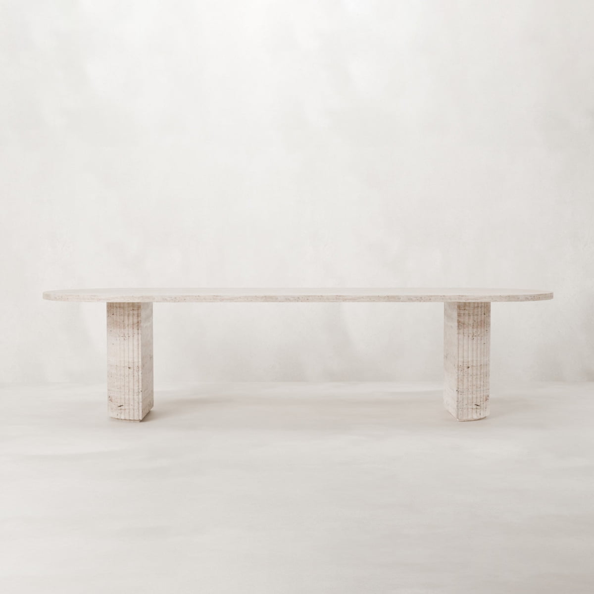 The Richmond Table is a minimalist dining table crafted from light-colored natural travertine, featuring two block legs and a smooth, flat top—an elegant sculptural statement for any neutral space.