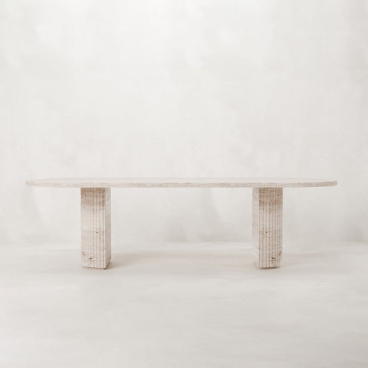 The Richmond Table features a minimalist travertine surface and two textured rectangular legs, displayed on a plain white background—ideal as a sculptural statement piece for any modern interior.