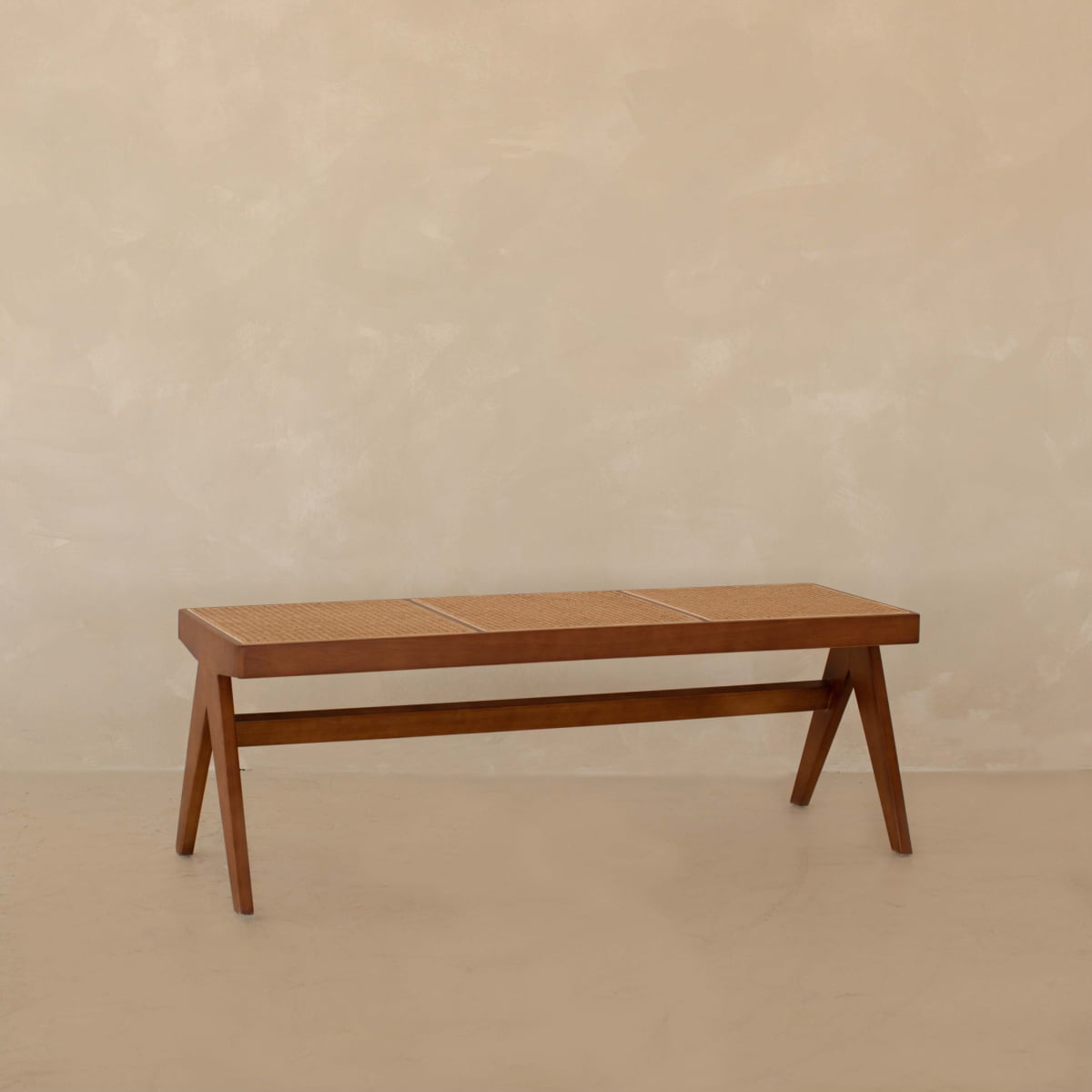 The Rivini Bench features angled legs and cane seat detailing, showcasing Scandinavian design against a beige textured wall and floor.