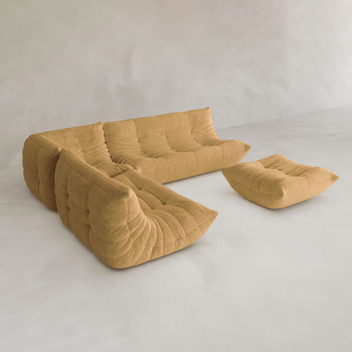 The Rolo Lounge Four Piece Sofa, a modern tan sectional with a modular system and matching ottoman, features tufted plush design and deep cushions. It sits on a light minimalist floor against a plain, light-colored wall.