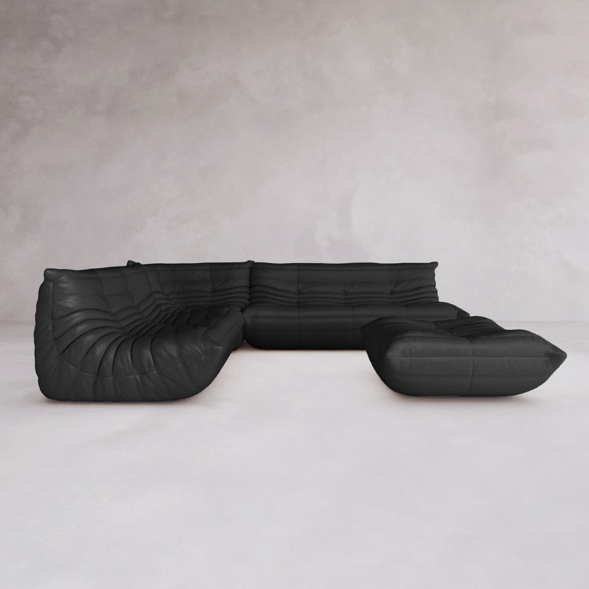 The Rolo Lounge Four Piece Sofa, a modular black sectional with plush tufted cushions, sits in an empty room with light walls and a pale floor, highlighting its sleek mid-century-inspired design.