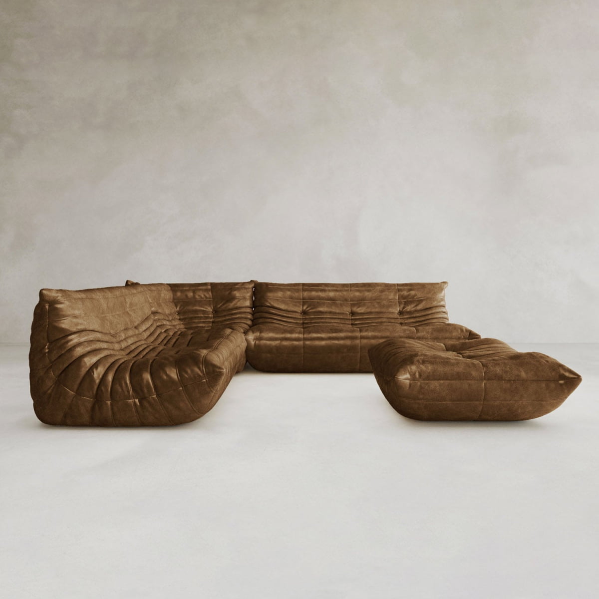 The Rolo Lounge Four Piece Sofa, a spacious brown leather modular sectional with deep, plush cushions, highlights contemporary design on a light floor beside a neutral textured wall.