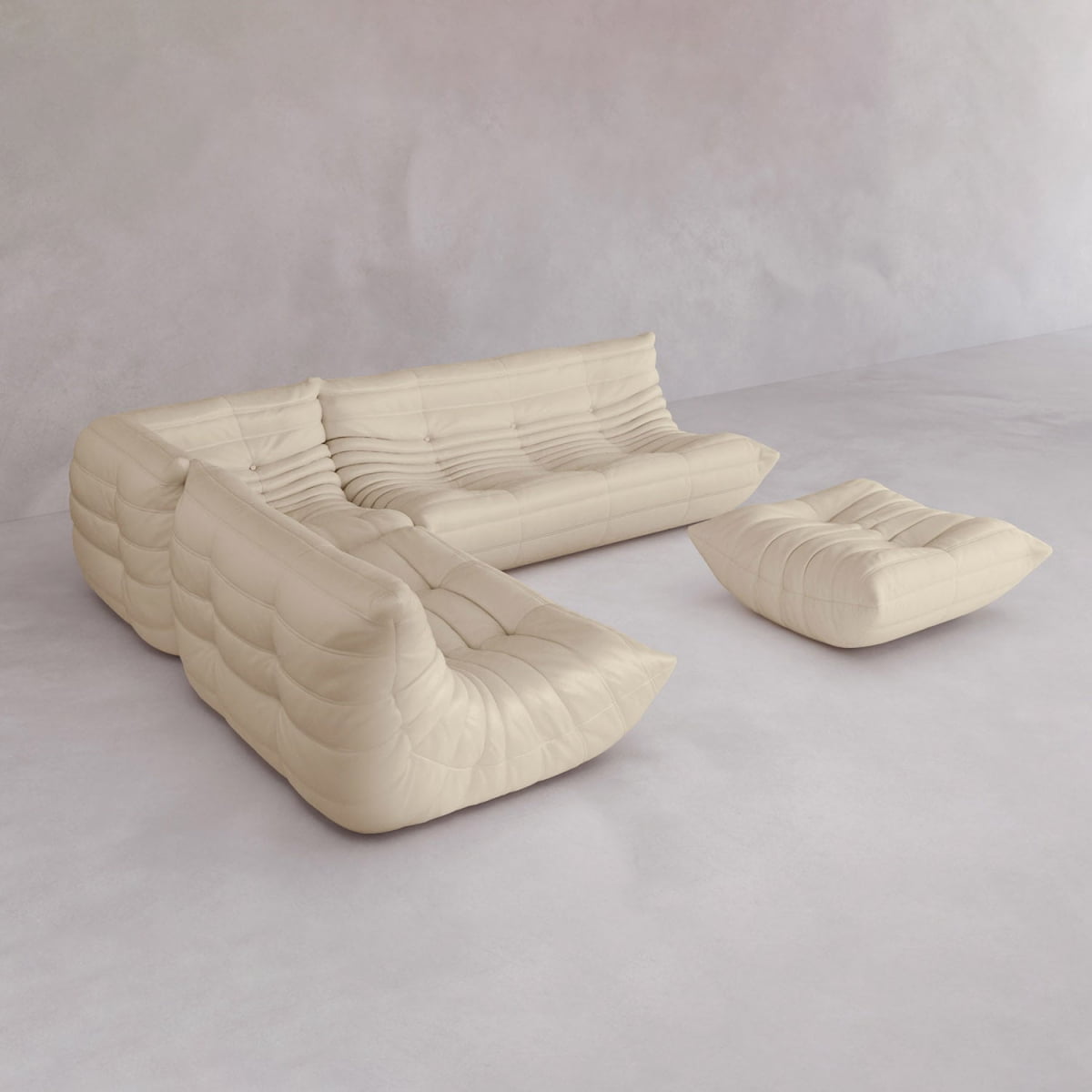 The Rolo Lounge Four Piece Sofa features a modern, cream-colored, tufted design with plush upholstery and mid-century style. Arranged in an L-shape with a matching ottoman, it sits against a minimalist light gray backdrop.