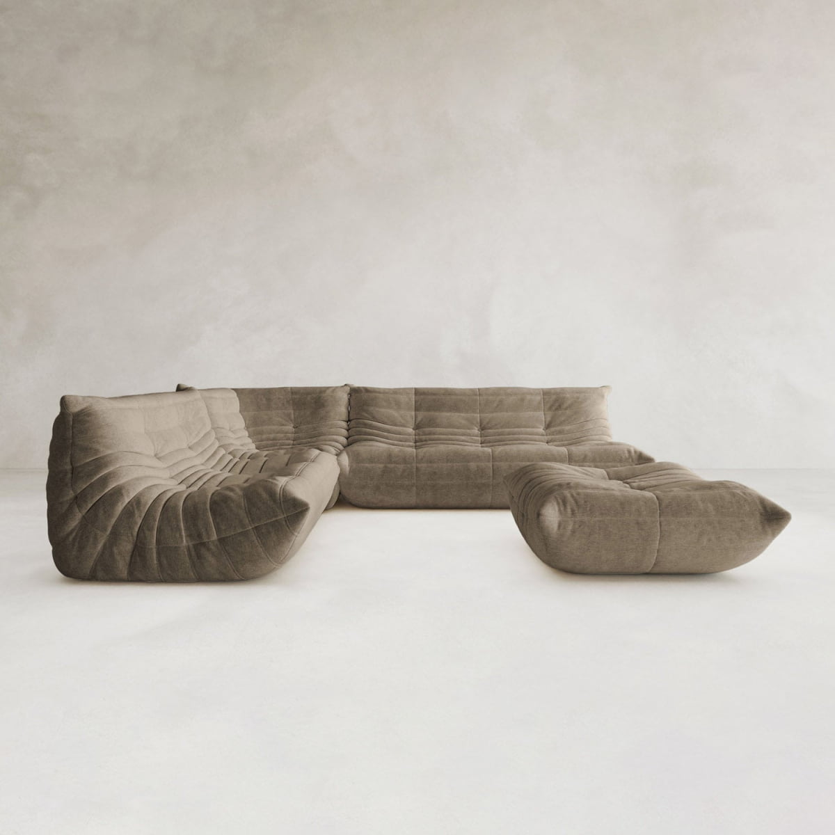 The Rolo Lounge Four Piece Sofa, with its modern U-shaped design, deep seats, and soft tufted brown fabric, sits in a spare minimalist room—its modular system offers flexible arrangements with subtle mid-century style.
