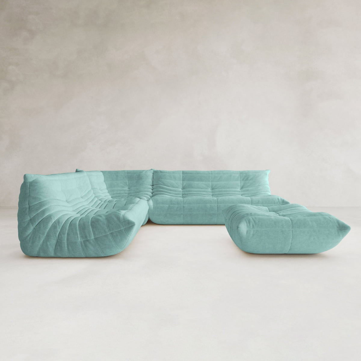 The Rolo Lounge Four Piece Sofa, a modern light blue modular sectional with a low profile and plush tufted cushions inspired by mid-century design, stands in an empty room with light walls and flooring.