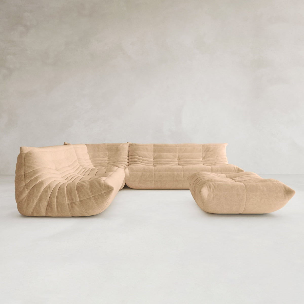 The Rolo Lounge Four Piece Sofa, a modern beige modular sectional with tufted plush cushions, anchors this minimalist space with light gray textured walls, a smooth white floor, and subtle mid-century design touches.