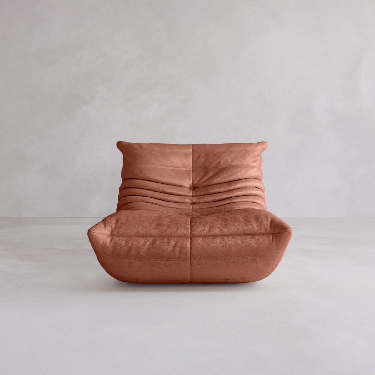 The Rolo Lounge Sofa Chair with Ottoman features a 70s-inspired, low, armless design in soft brown leather with horizontal pleats, channeling mid-century style against a plain light gray background.