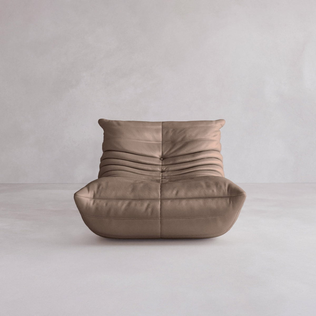 The Rolo Lounge Sofa Chair with Ottoman features a modern, armless design inspired by mid-century style, soft tan-brown leather upholstery with ruched detailing, and a low, wide seat against a plain light gray wall and floor.