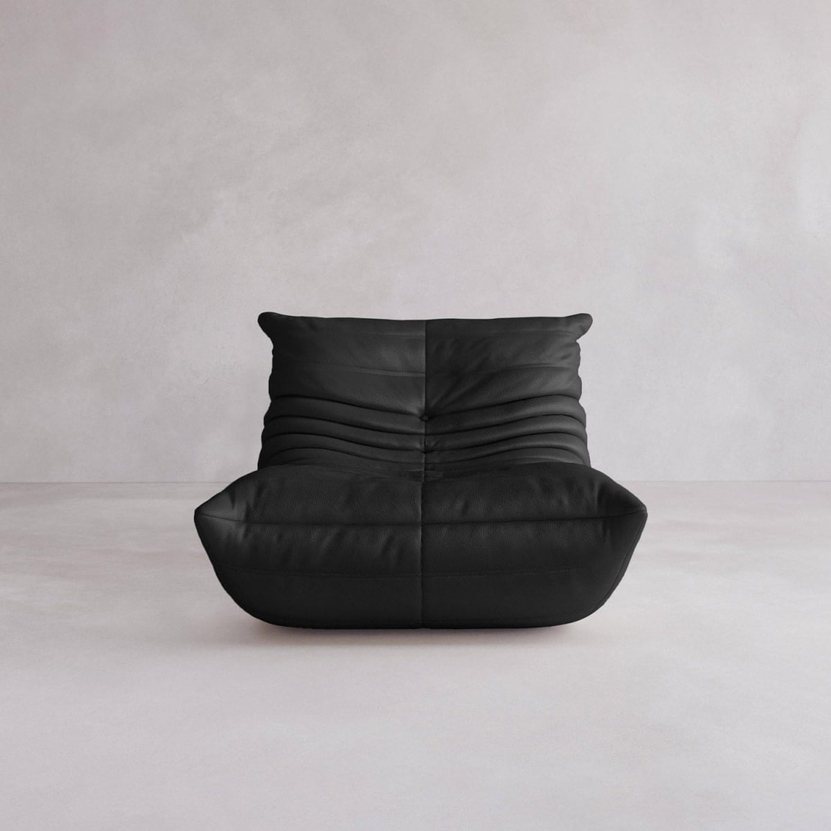 The Rolo Lounge Sofa Chair with Ottoman, a modern armless black leather piece with soft pleated upholstery and mid-century design, sits on a light gray floor against a textured light gray wall.