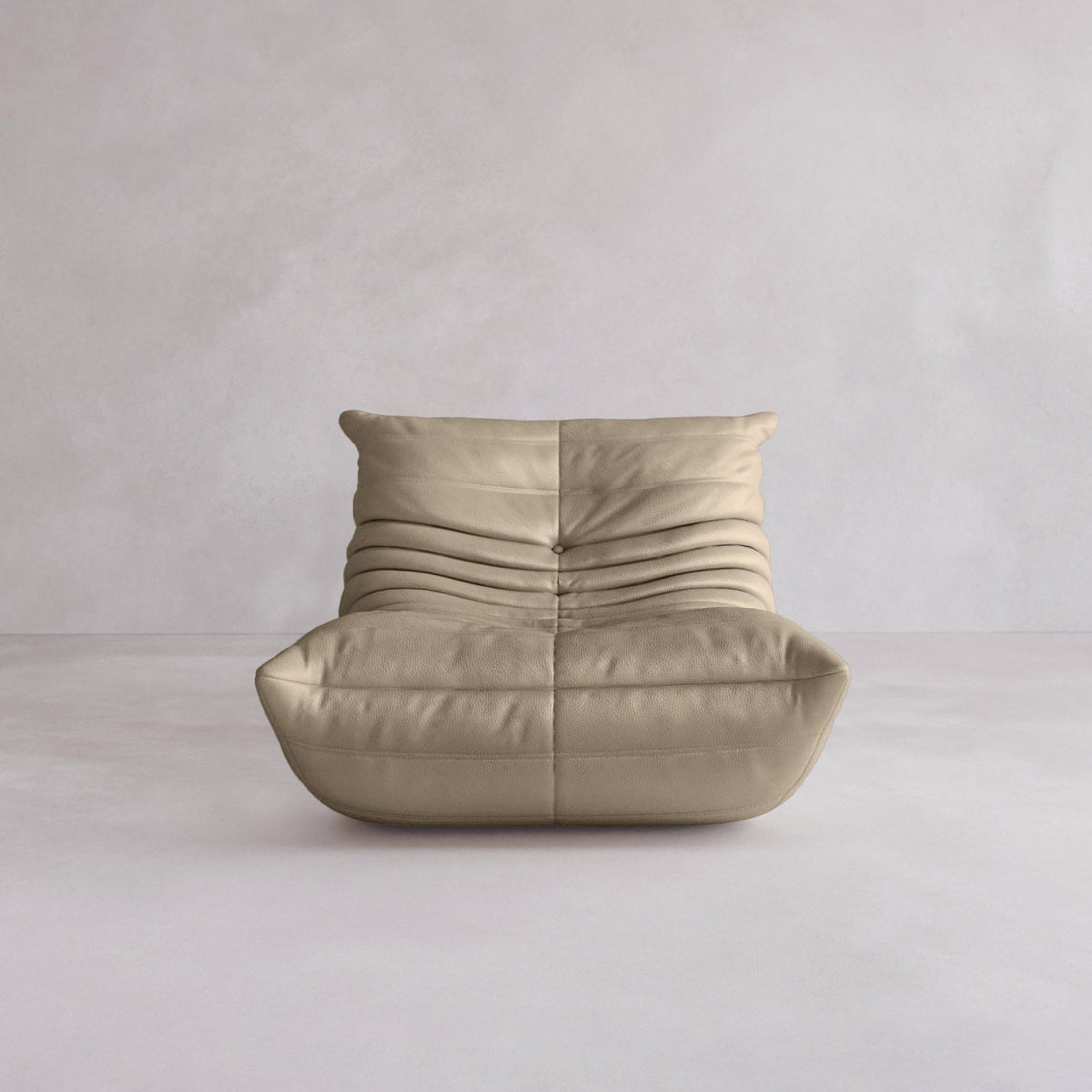 The Rolo Lounge Sofa Chair with Ottoman, an armless beige seat featuring soft, cushioned folds and mid-century inspiration, sits on a light gray floor against a plain light gray wall.