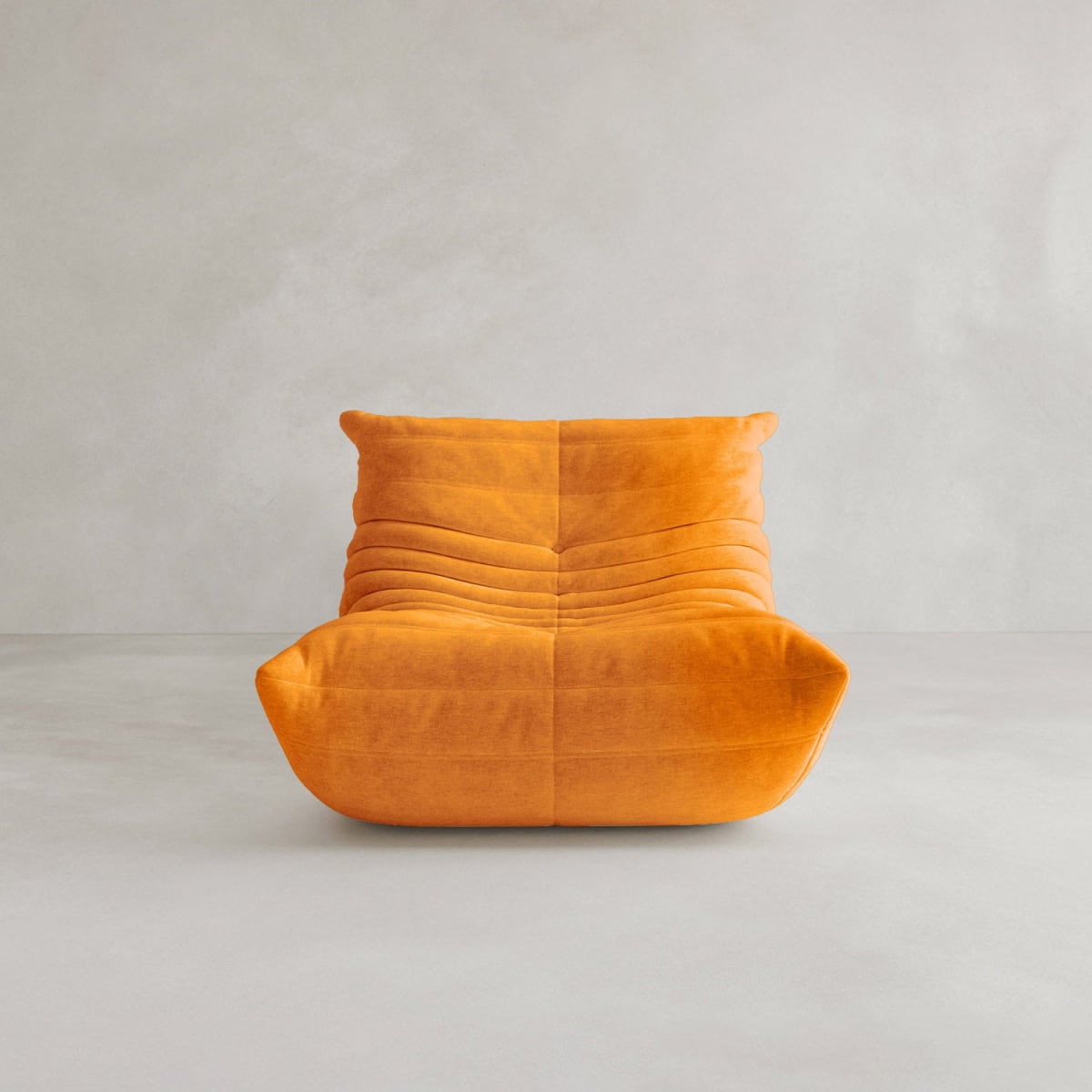 The Rolo Lounge Sofa Chair with Ottoman features a modern, low-profile orange design with segmented texture, echoing mid-century style as it sits on a light grey floor against a plain grey wall.