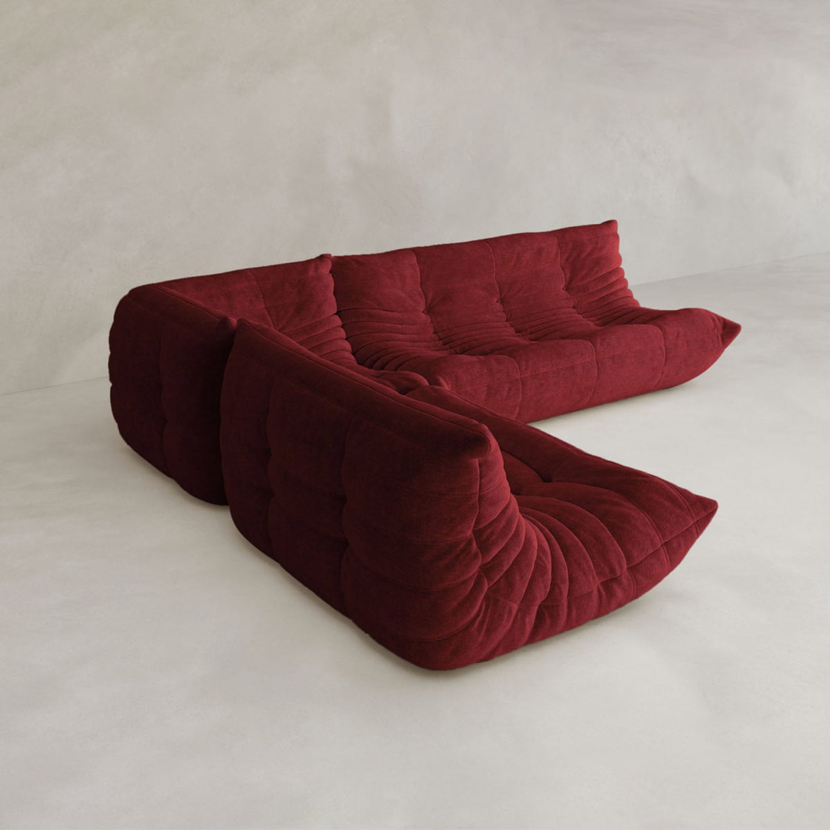 The Rolo Lounge Three Piece Sofa is a modern, modular sectional in deep red with soft tufted cushions and a legless look, inspired by mid-century design. Shown against a minimalist, light-colored background.