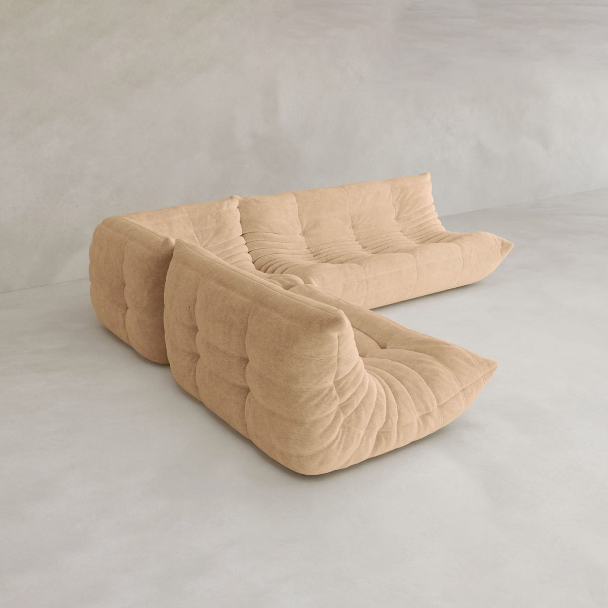 The Rolo Lounge Three Piece Sofa, a tan modular L-shaped design with plush tufted cushions, exemplifies contemporary style as it rests on a light grey floor against a matching wall.