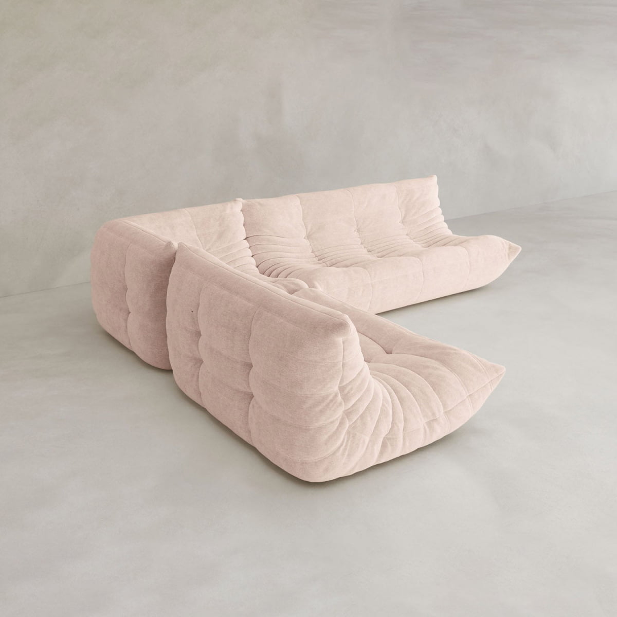 The Rolo Lounge Three Piece Sofa is a modern, modular sectional in light beige with deep tufted cushions, arranged L-shaped on a gray concrete floor against a pale textured wall for subtle mid-century charm.