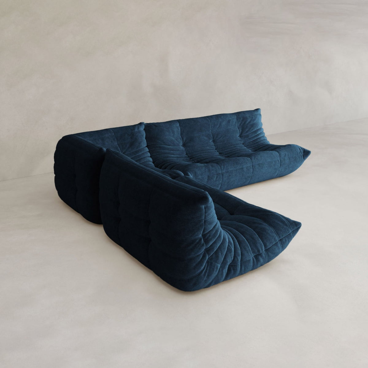 The Rolo Lounge Three Piece Sofa, a modern modular L-shaped sectional in deep blue with plush tufted cushions, sits on a light beige floor against a textured neutral wall.